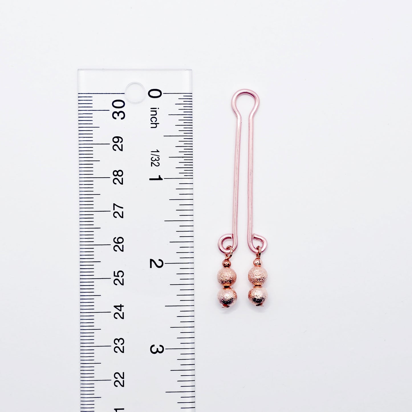 Rose Gold Labia Clip Next to ruler on white background