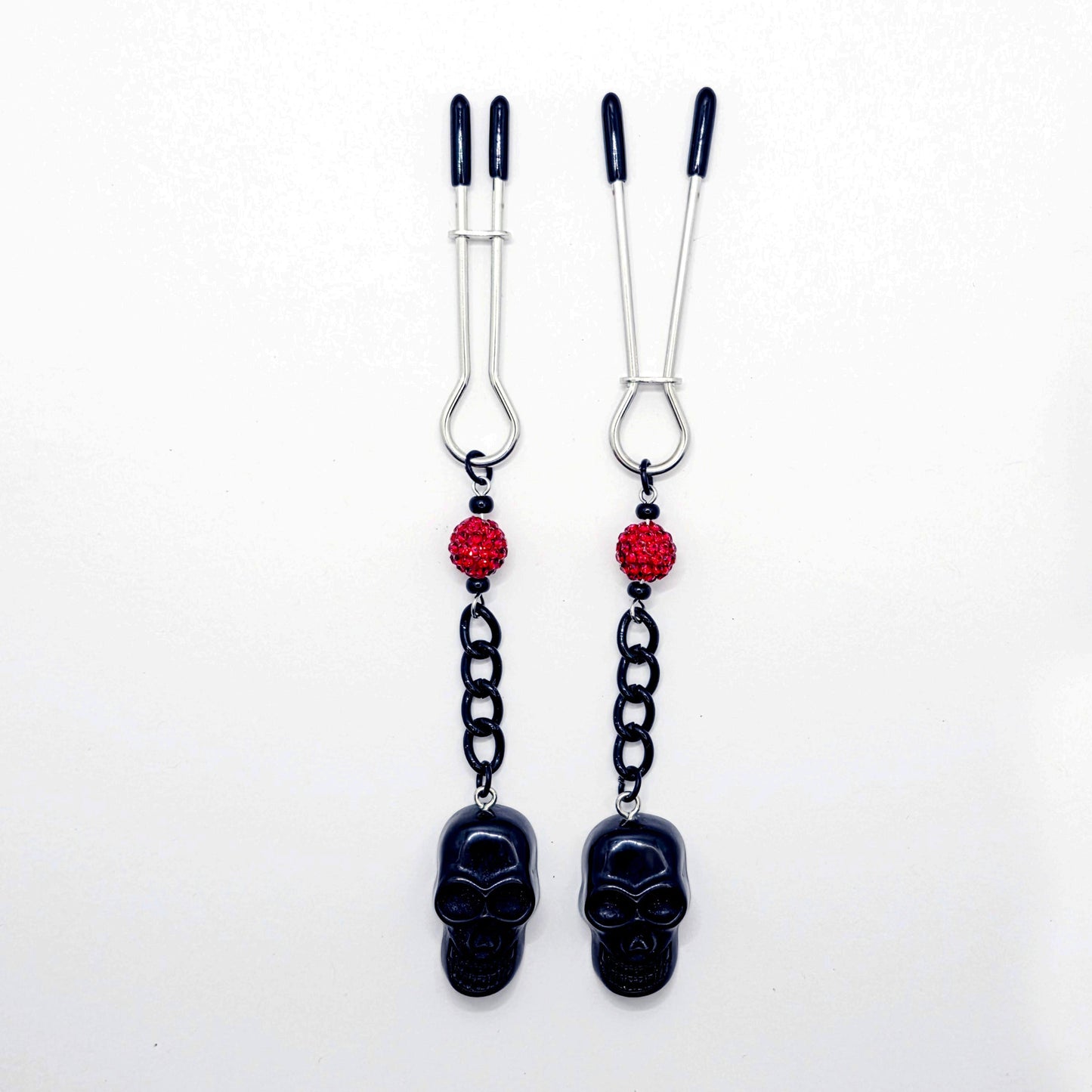 Pair of black skull Nipple Clamps with red beads on a white background