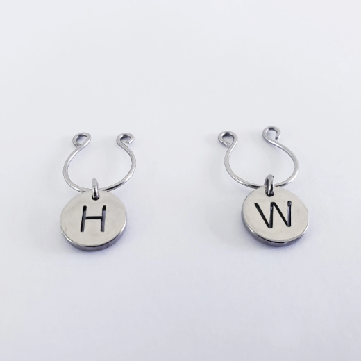A pair of stainless steel non-piercing nipple rings with attached circular tags, one tagged with 'H' and the other with 'W'.