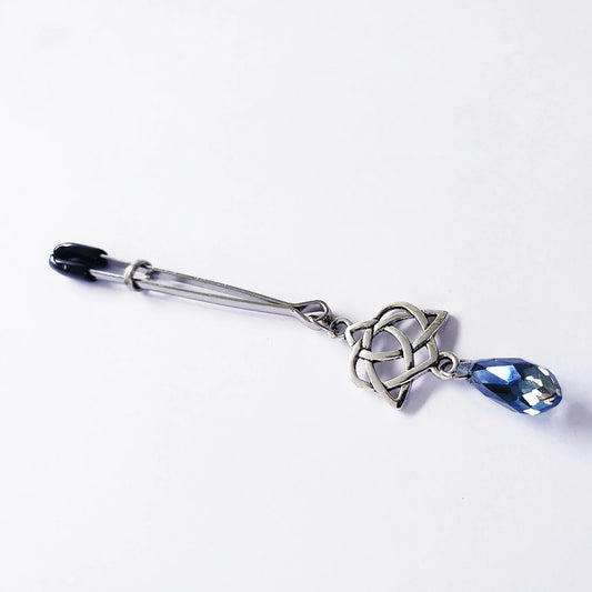 A silver clitoral clamp with a Celtic Triquetra and heart design, featuring a blue crystal on the end.