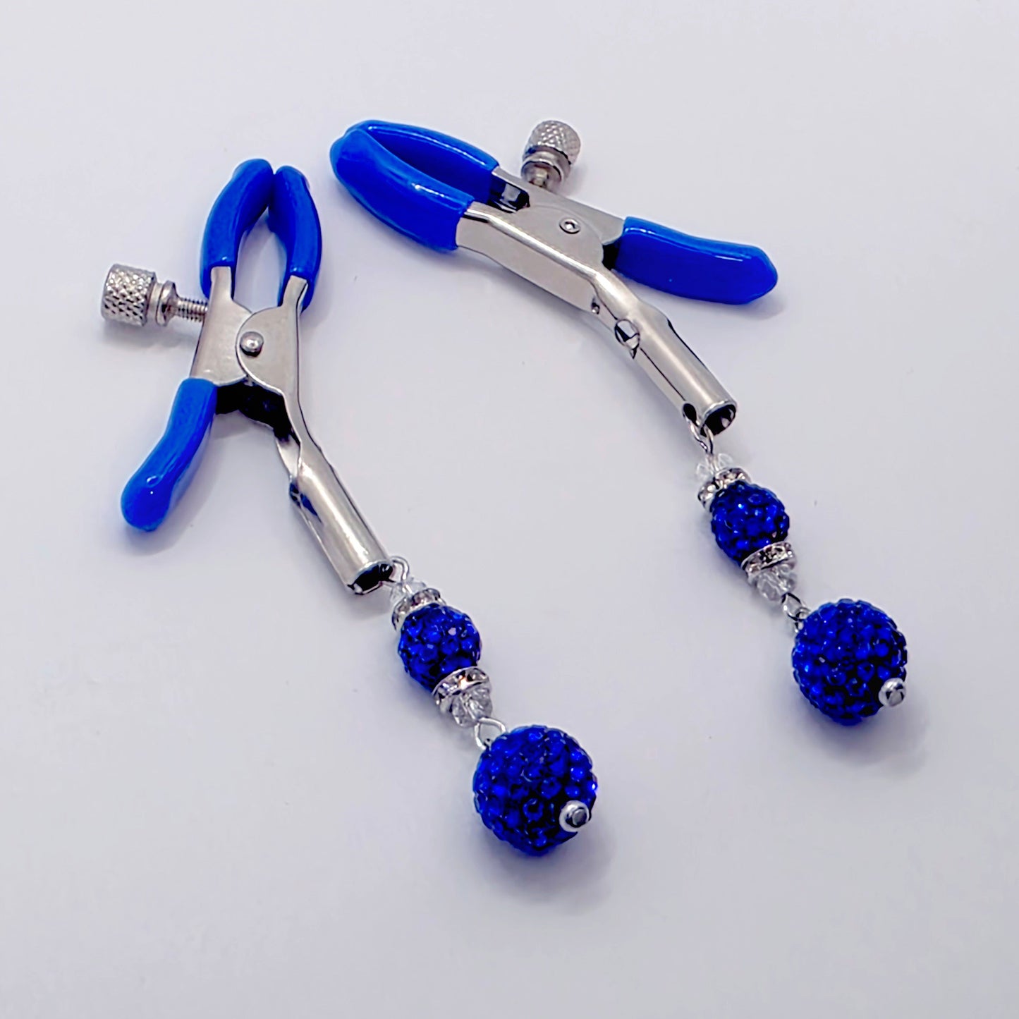 Metal clamps with blue handles and embellished with blue gemstones on a white background