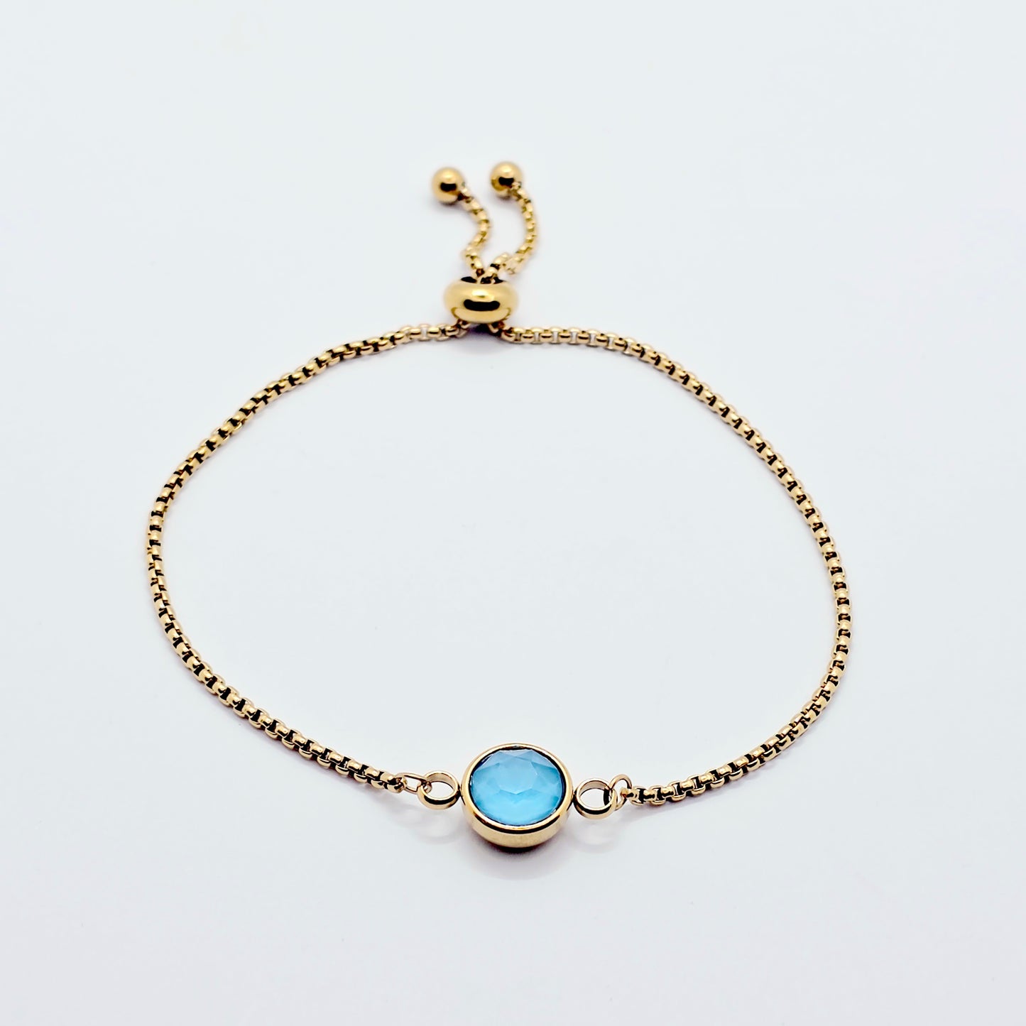 Gold penis bracelet with a blue gemstone on a white background