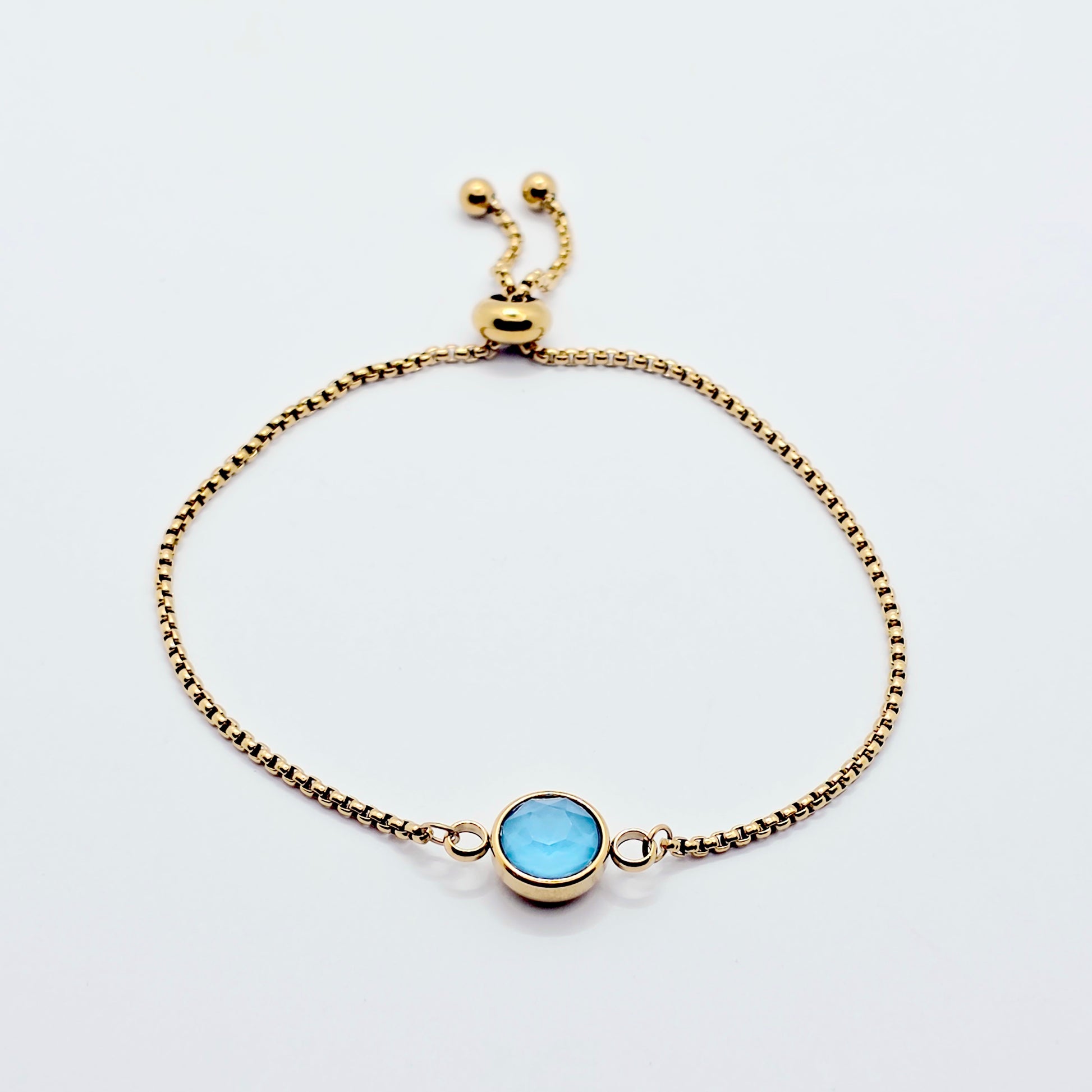 Gold penis bracelet with a blue gemstone on a white background