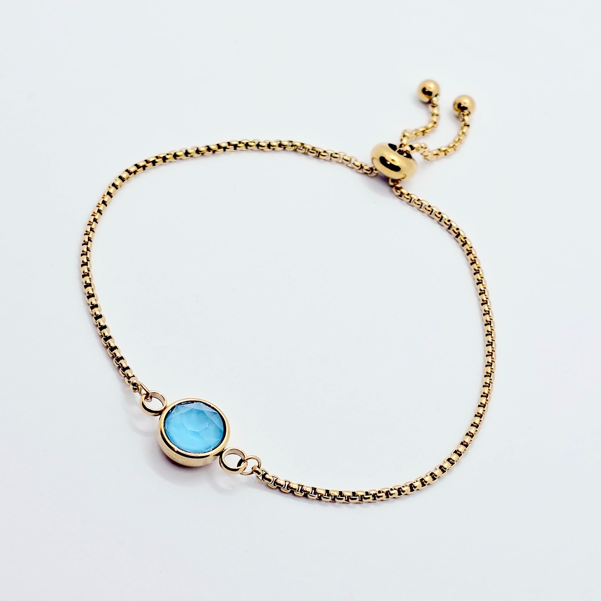 Gold penis bracelet with a blue gemstone on a white background
