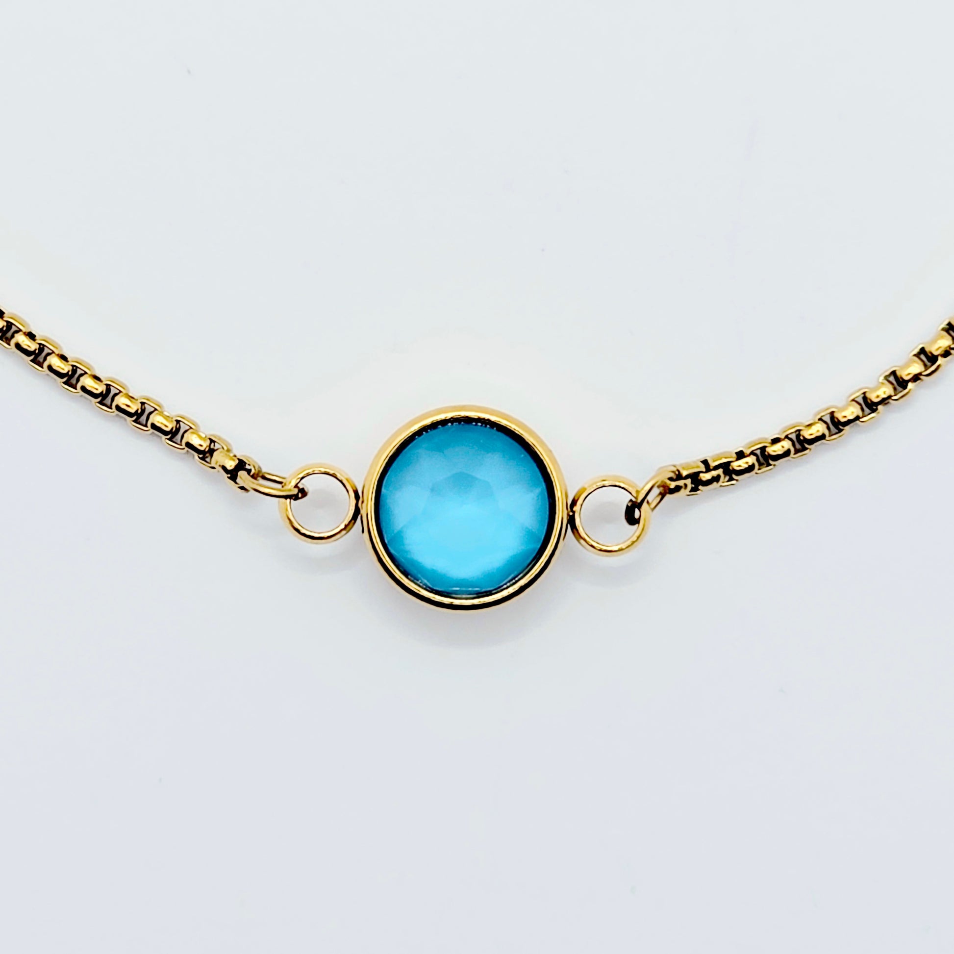 Gold penis bracelet with a blue gemstone on a light gray background