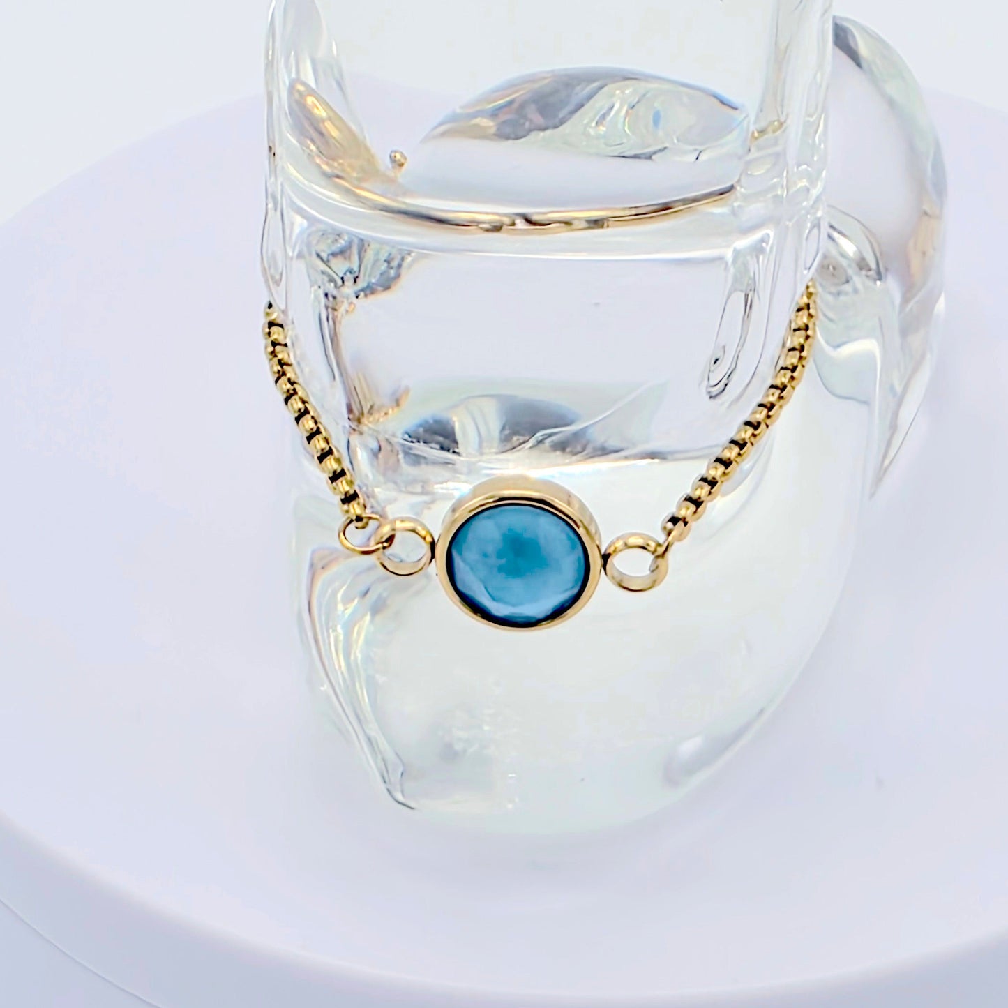Jewelry with a blue gemstone and gold chain on a white stand