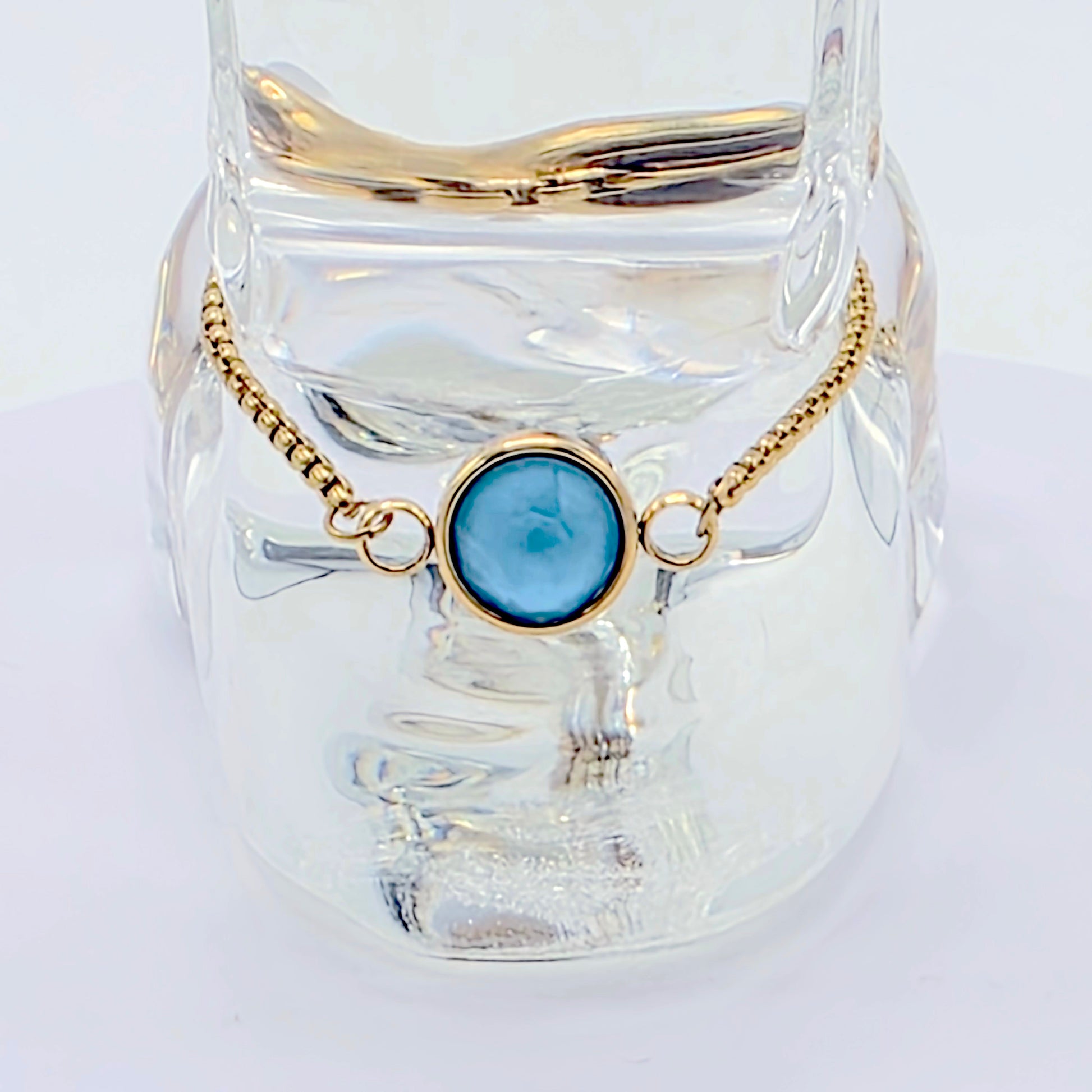 Gold bracelet with a blue stone on a clear glass stand