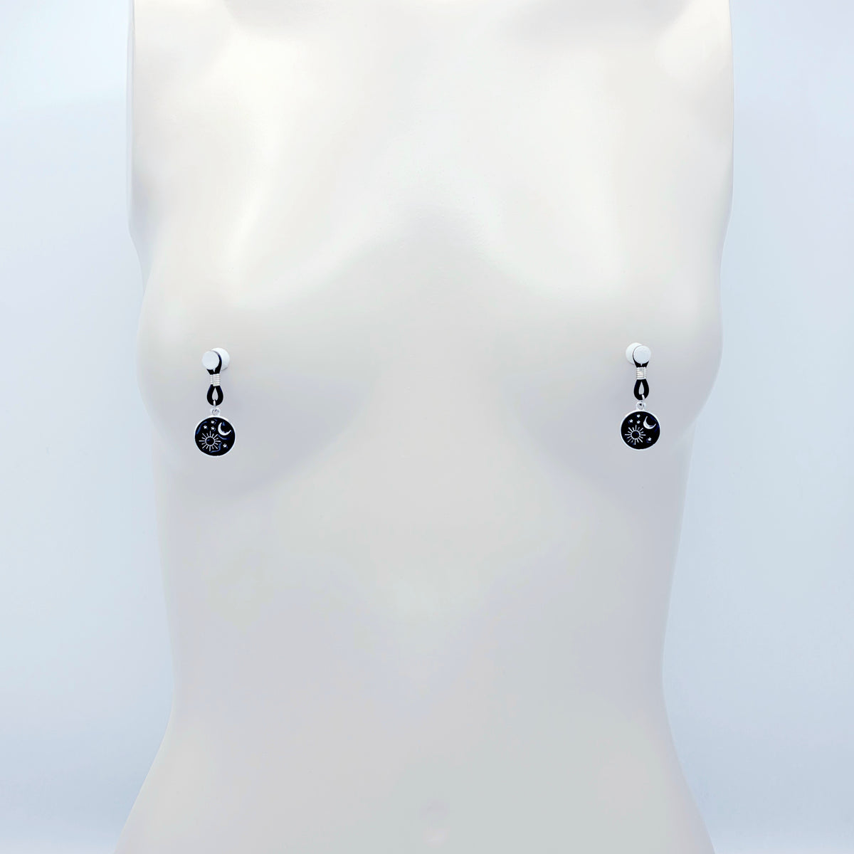pair of small black nipple nooses with circular celestial charms featuring a crescent moon, sun, and stars on a light gray background.