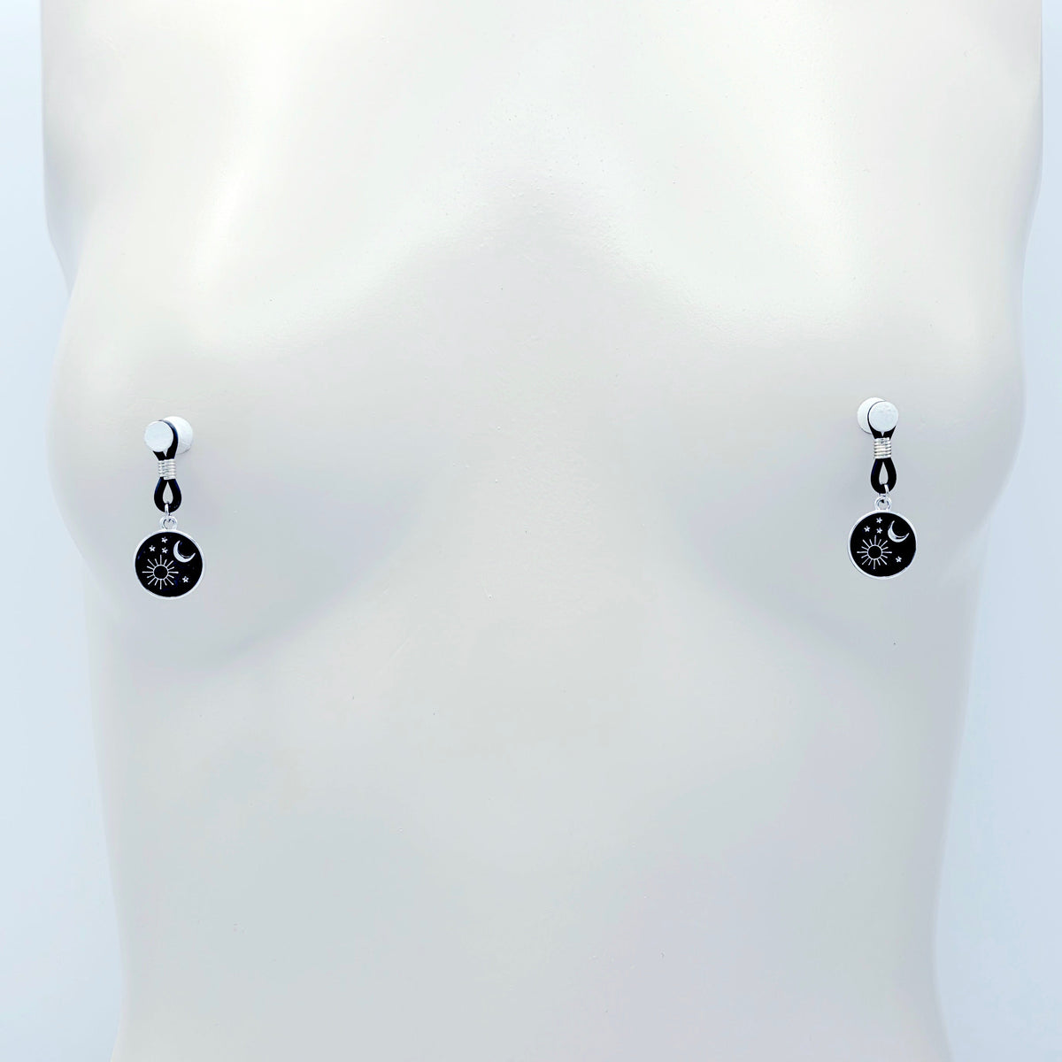 pair of small black nipple nooses with circular celestial charms featuring a crescent moon, sun, and stars on a light gray background.