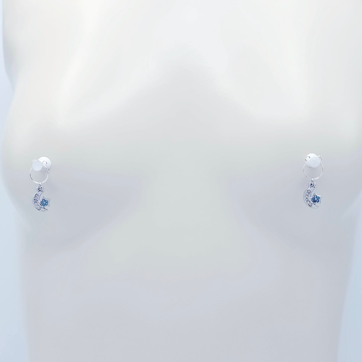 A pair of silver crescent moon and star dangle nipple rings with clear rhinestones and light blue star accents, shown on a plain light gray background.