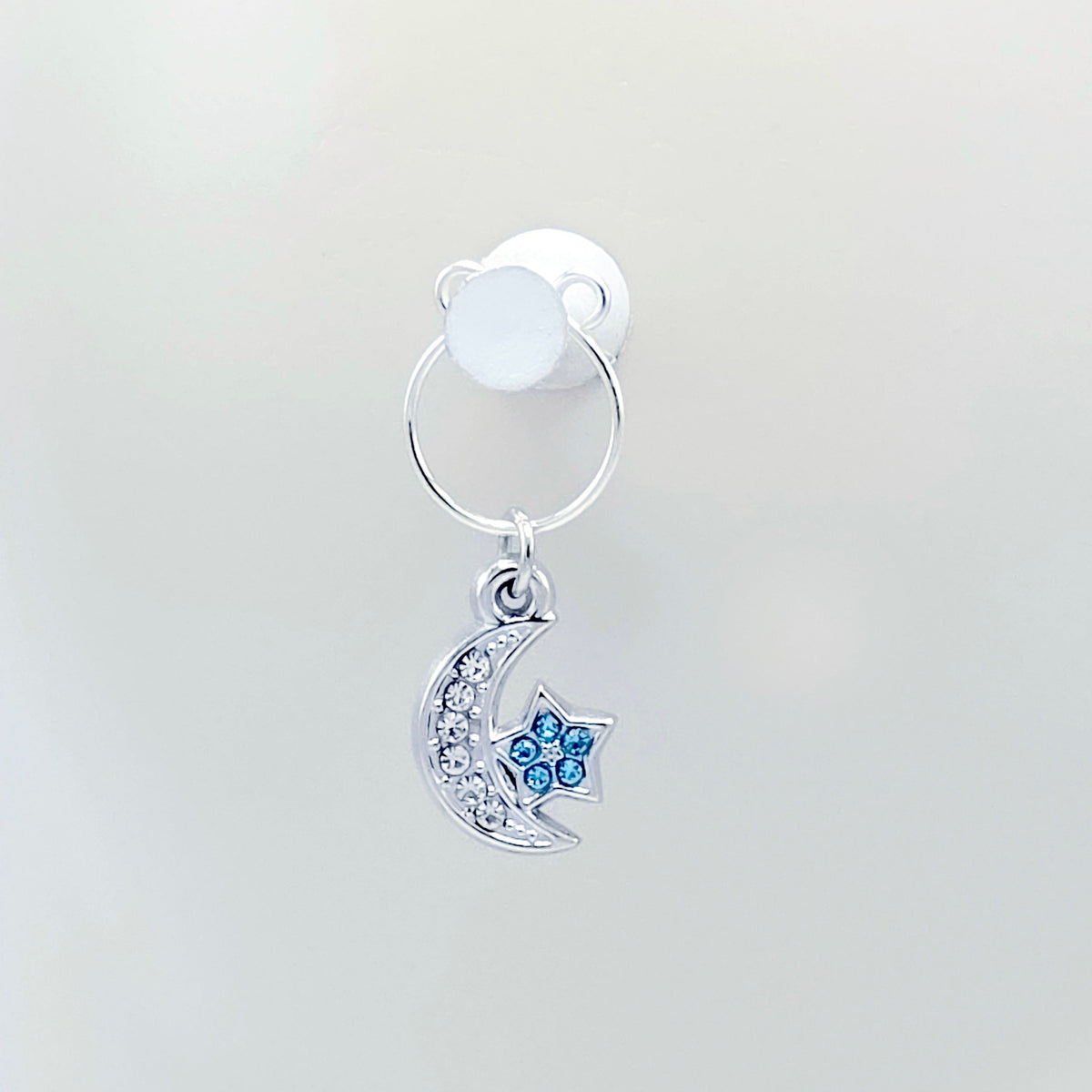 A pair of silver crescent moon and star dangle nipple rings with clear rhinestones and light blue star accents Hanging on tack