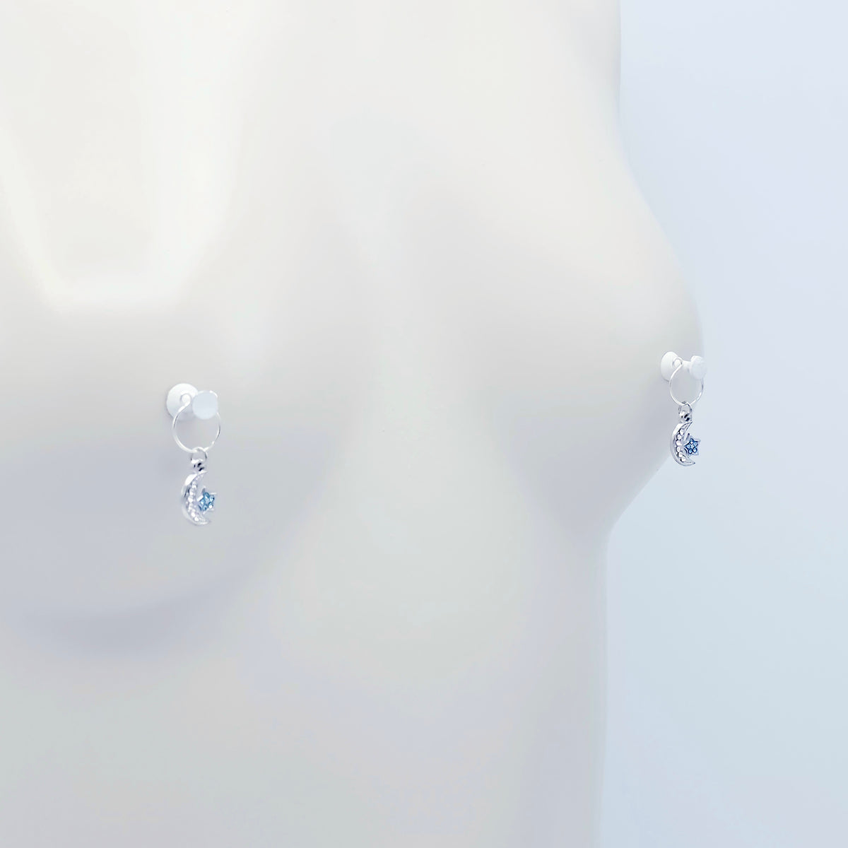 A pair of silver crescent moon and star dangle nipple rings with clear rhinestones and light blue star accents, shown on a mannequin. 
