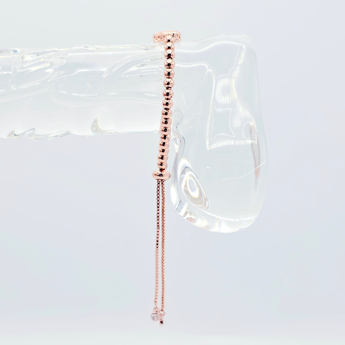 A delicate rose gold beaded chain earring with a long drop chain and a small clear crystal charm, displayed on a clear acrylic stand against a white background.