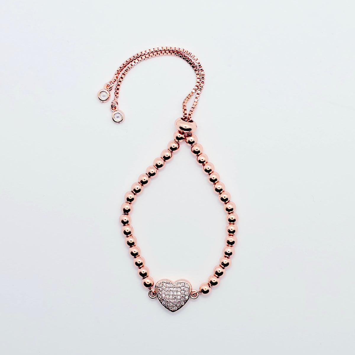 A rose gold beaded bracelet with a heart-shaped pavé charm, displayed on a clean white background.