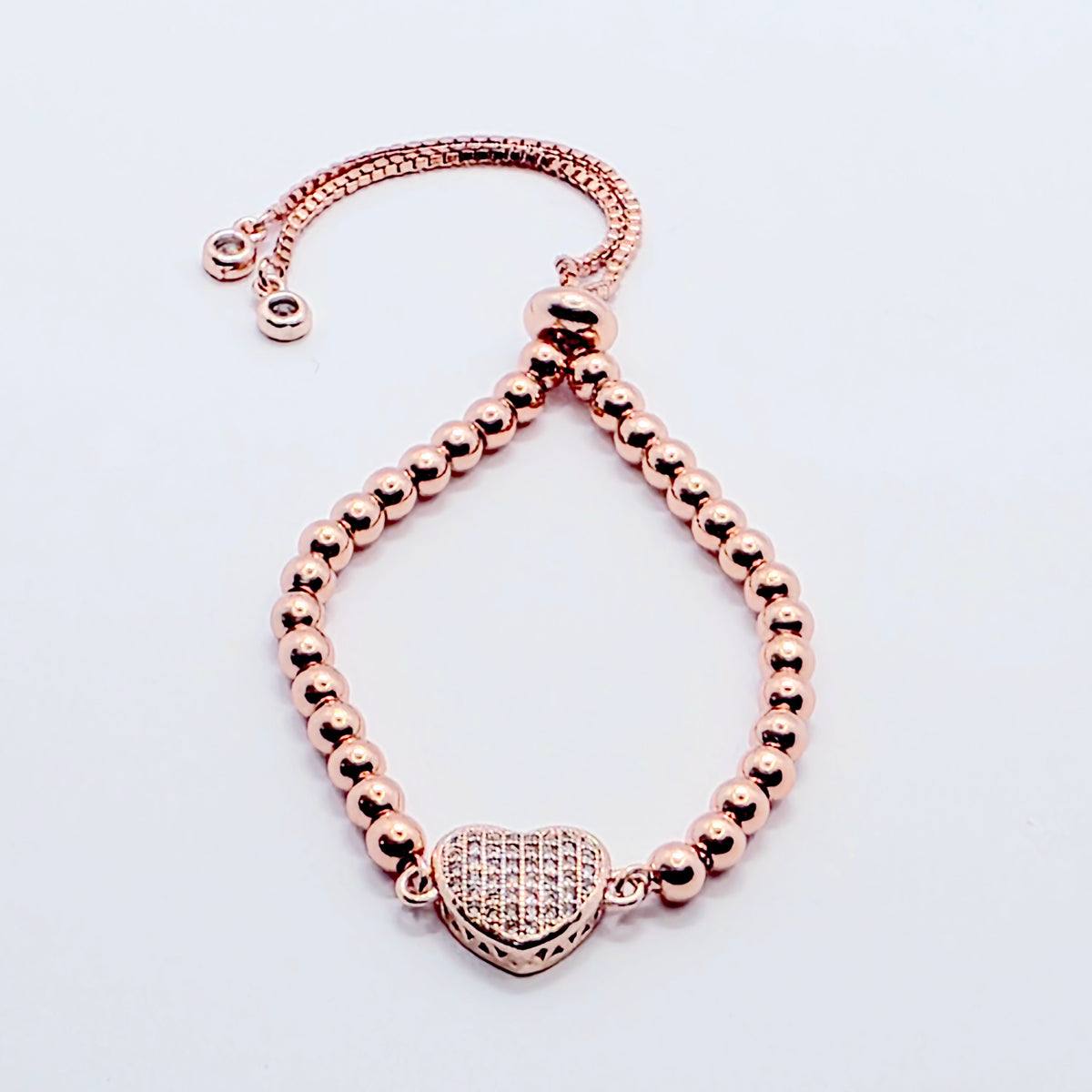 A rose gold beaded bracelet with a heart-shaped charm paved with small clear stones, displayed on a clean white background.