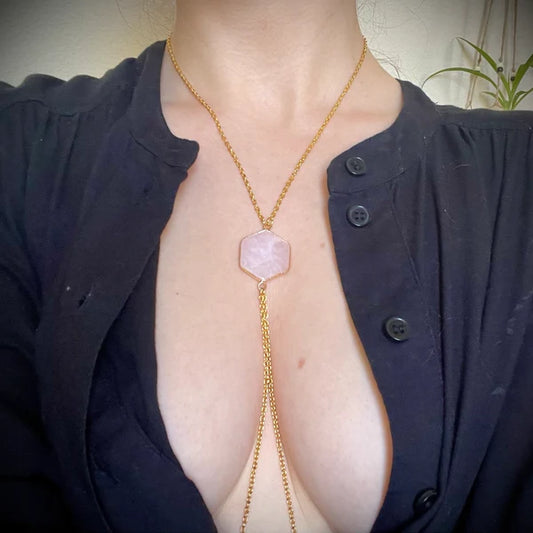 Person wearing a gold necklace with a pink rose quartz pendant, partially unbuttoned dark shirt.