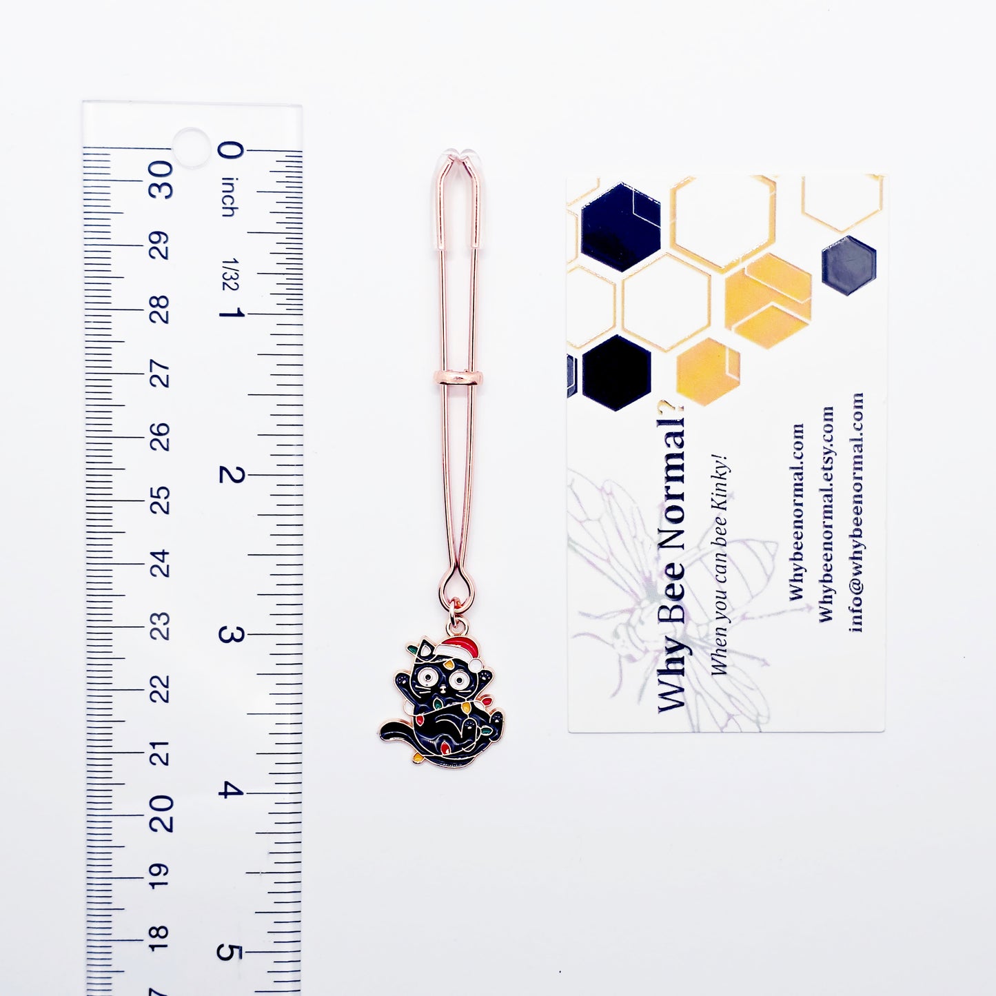 Rose Gold Tweezer Clit Clamp with Black Kitten Wrapped in Christmas Lights wearing a Santa Hat next to ruler and business card to show size