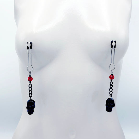 Pair of black skull Nipple Clamps with red beads on a white background