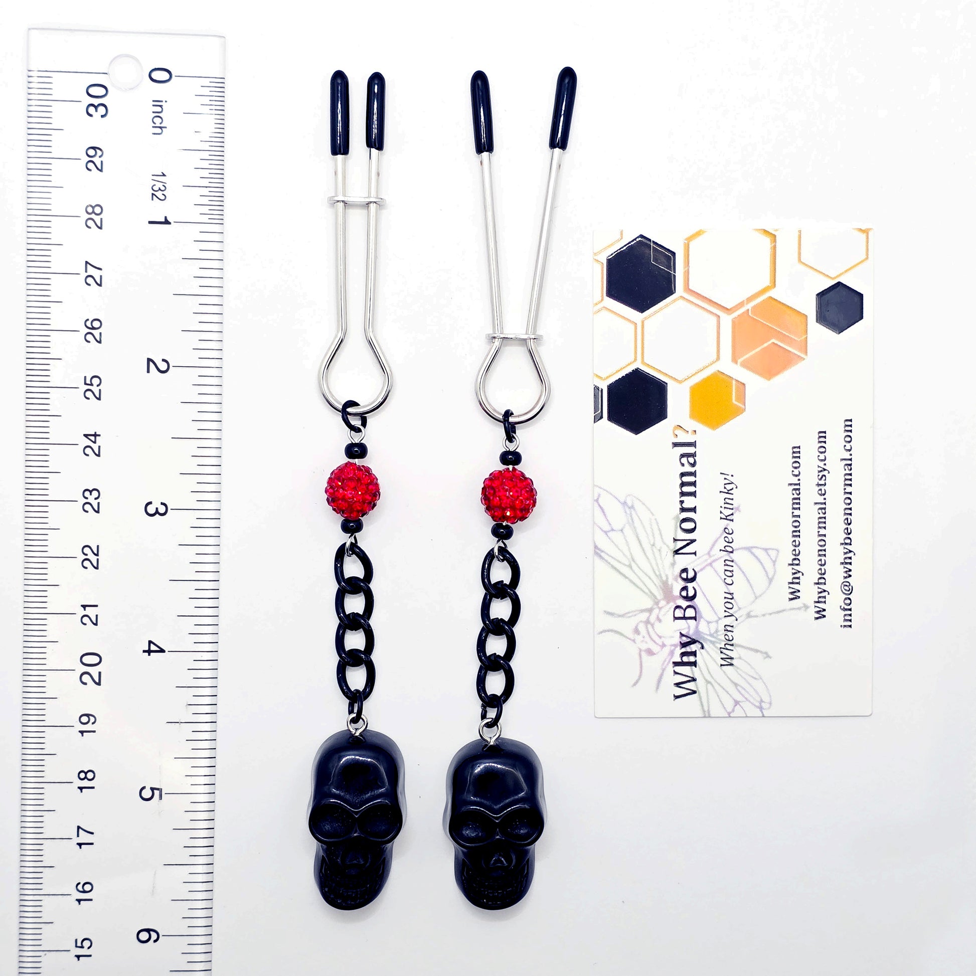 Pair of black skull Nipple Clamps with red beads on a white background