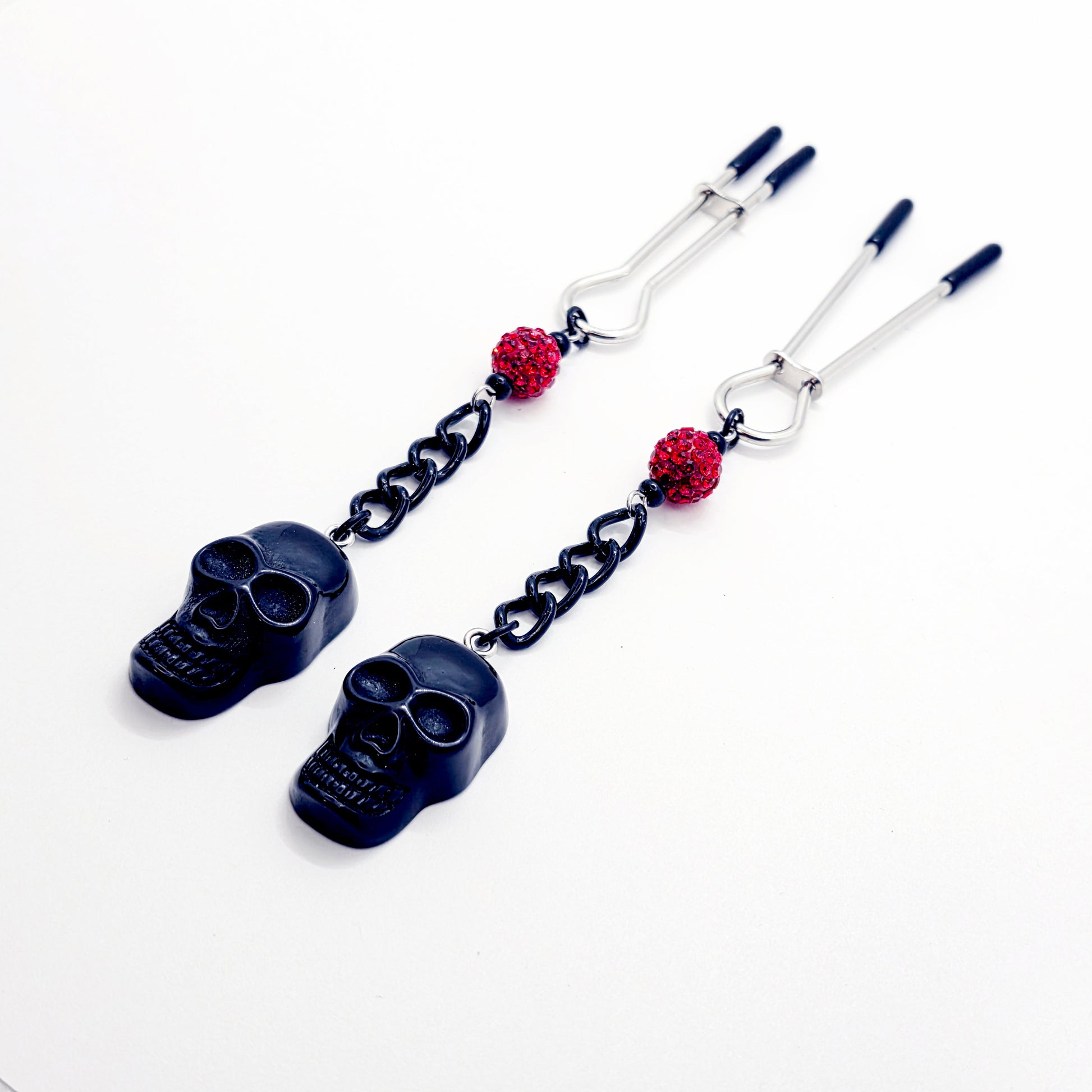Pair of black skull Nipple Clamps with red beads on a white background