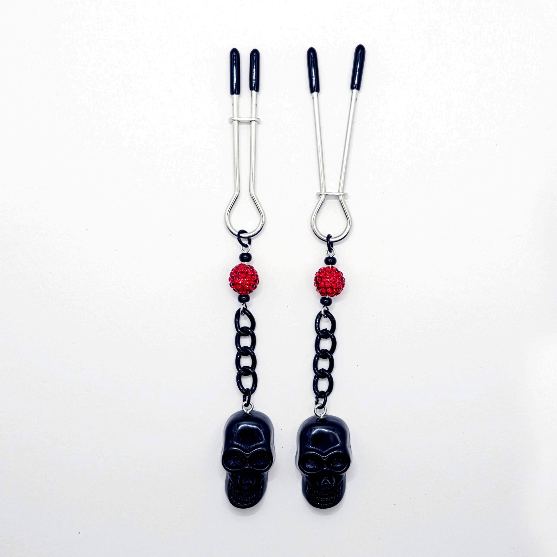 Pair of black skull Nipple Clamps with red beads on a white background