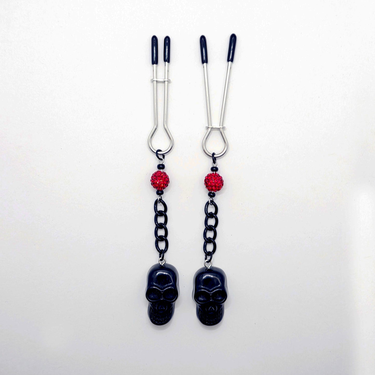 Pair of black skull Nipple Clamps with red beads on a white background