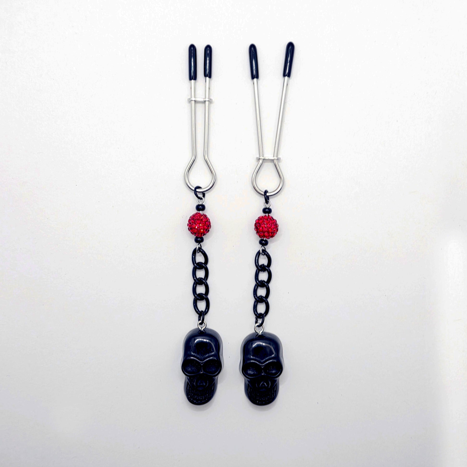Pair of black skull Nipple Clamps with red beads on a white background