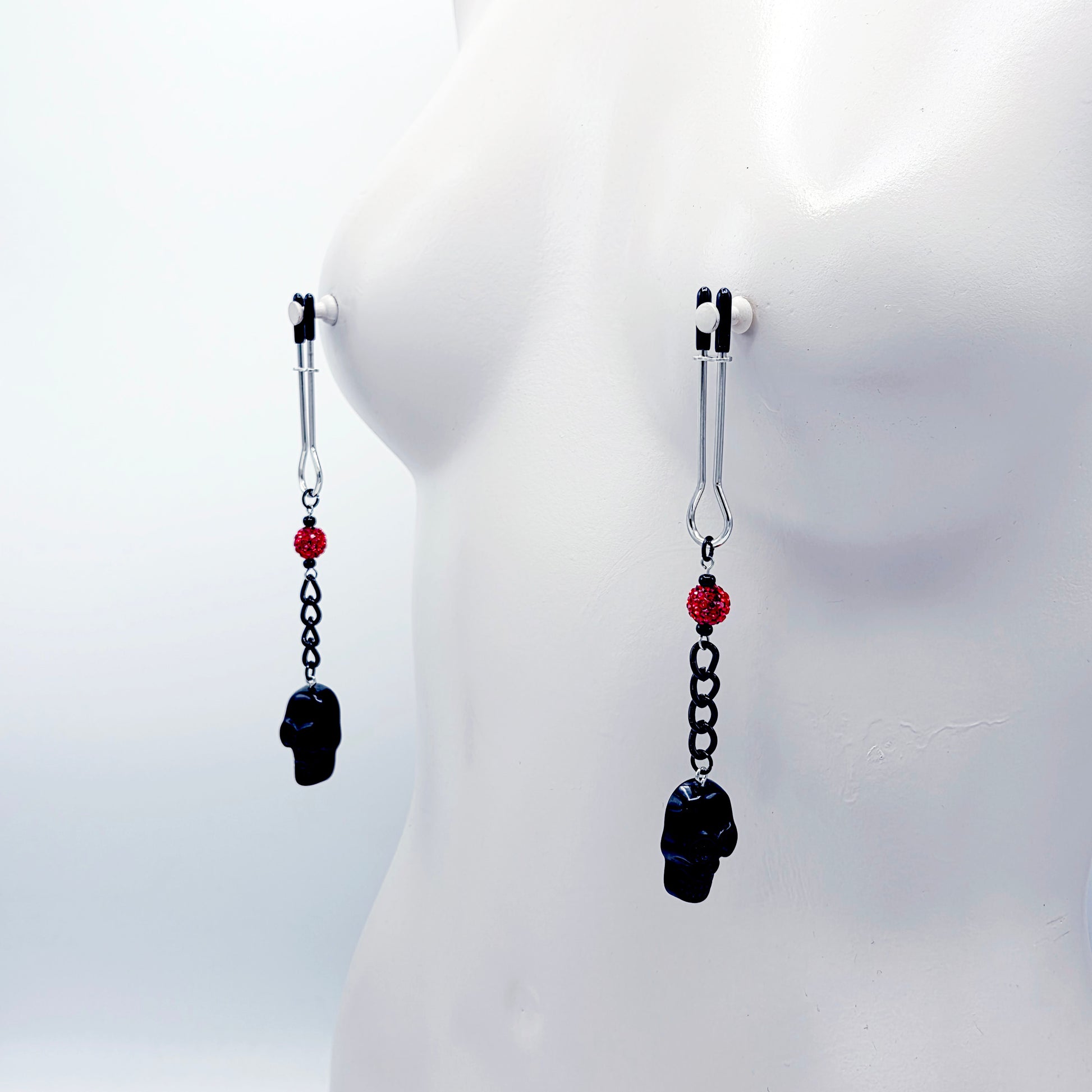 Pair of black skull Nipple Clamps with red beads on a white background