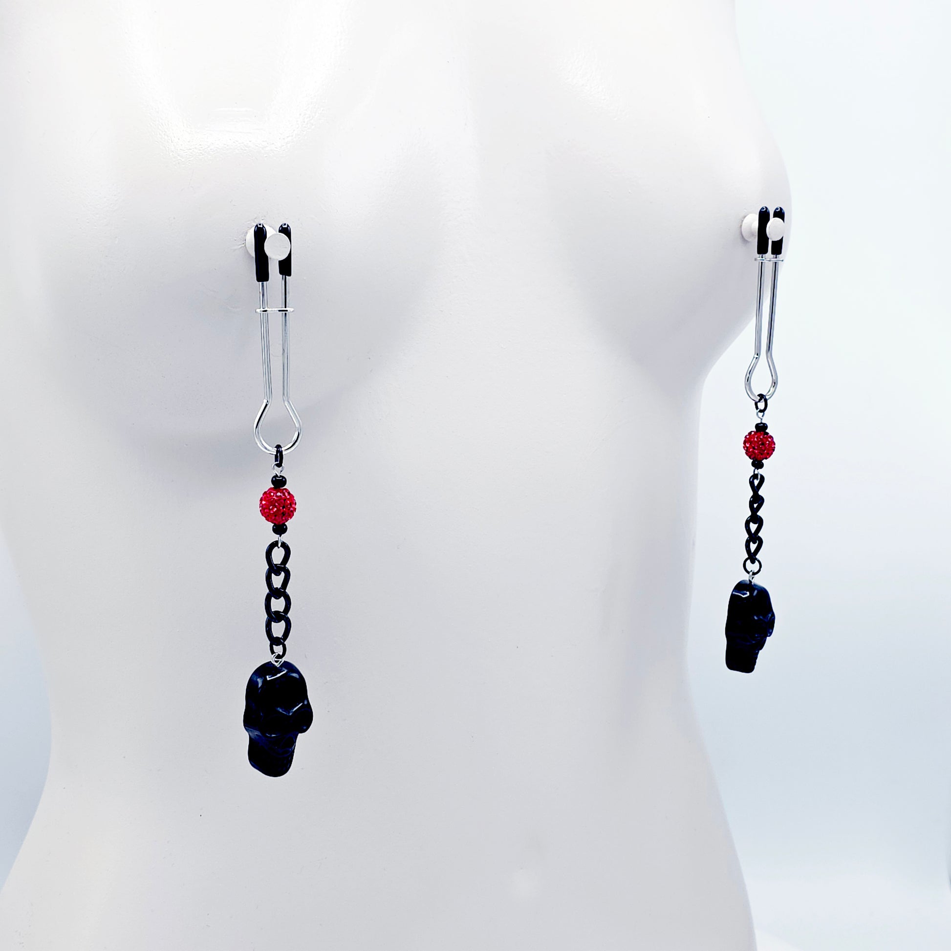 Pair of black skull Nipple Clamps with red beads on a white background